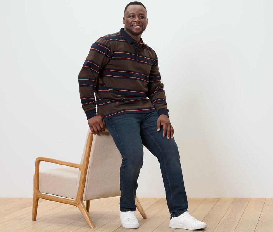 Muž sedí na stoličke a má na sebe polokošeľu s dlhými rukávmi.