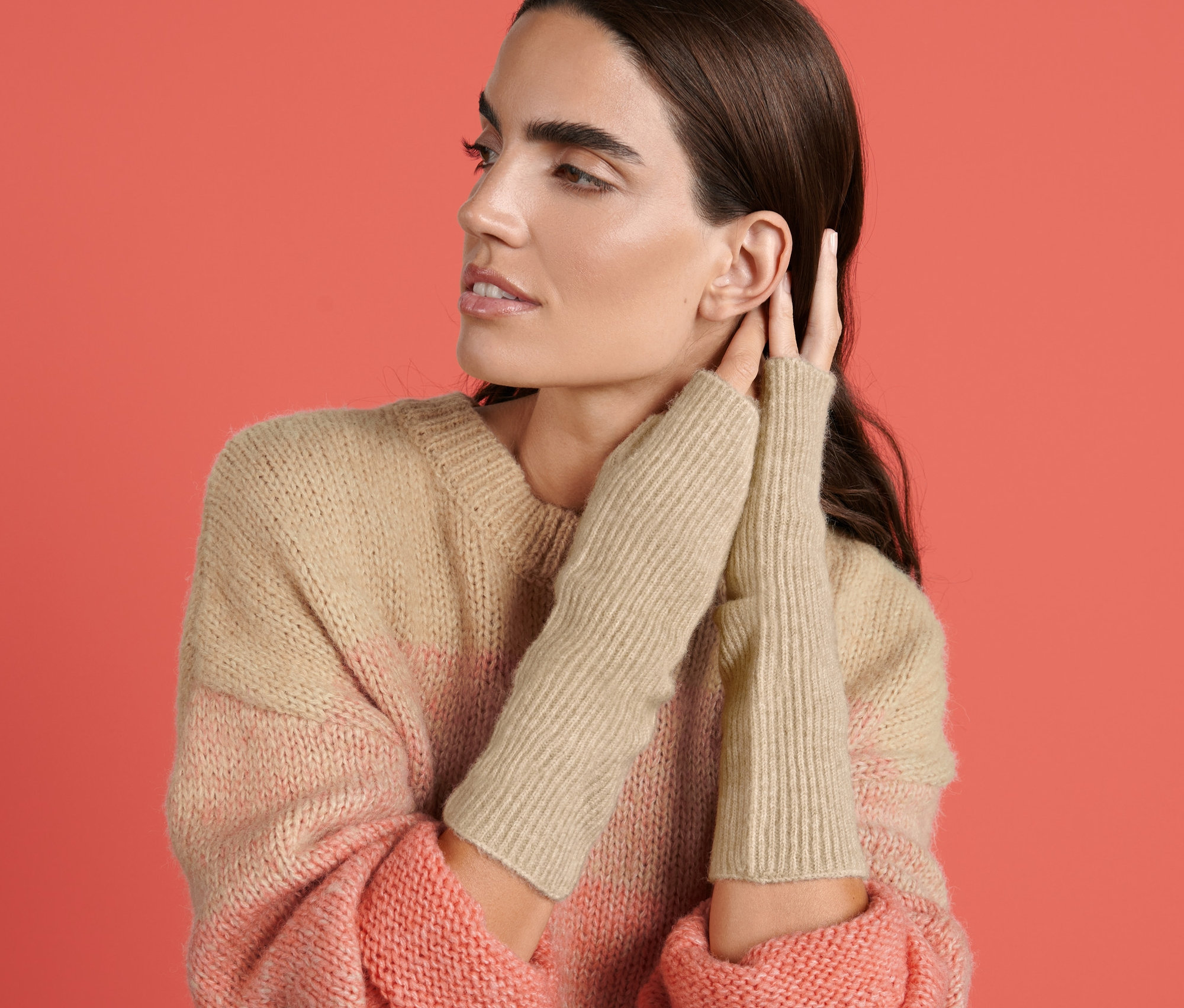 Žena sa dotýka ucha, má na sebe rebrované rukávniky a pruhovaný sveter.