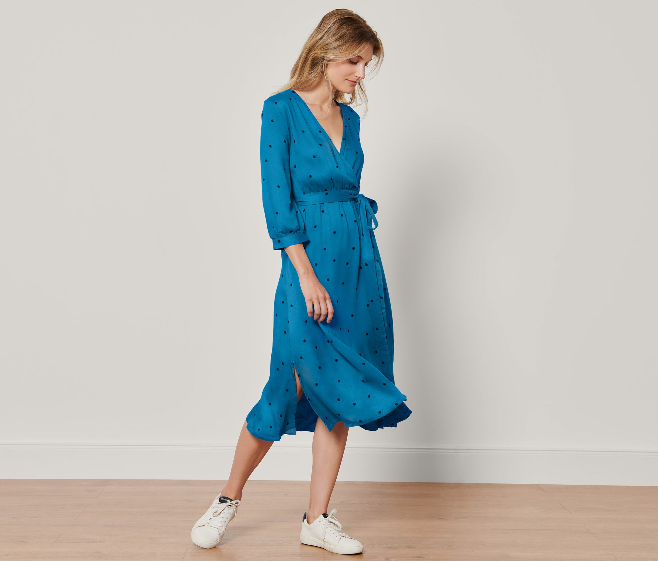 Žena stojí a má na sebe bodkované tkané šaty.