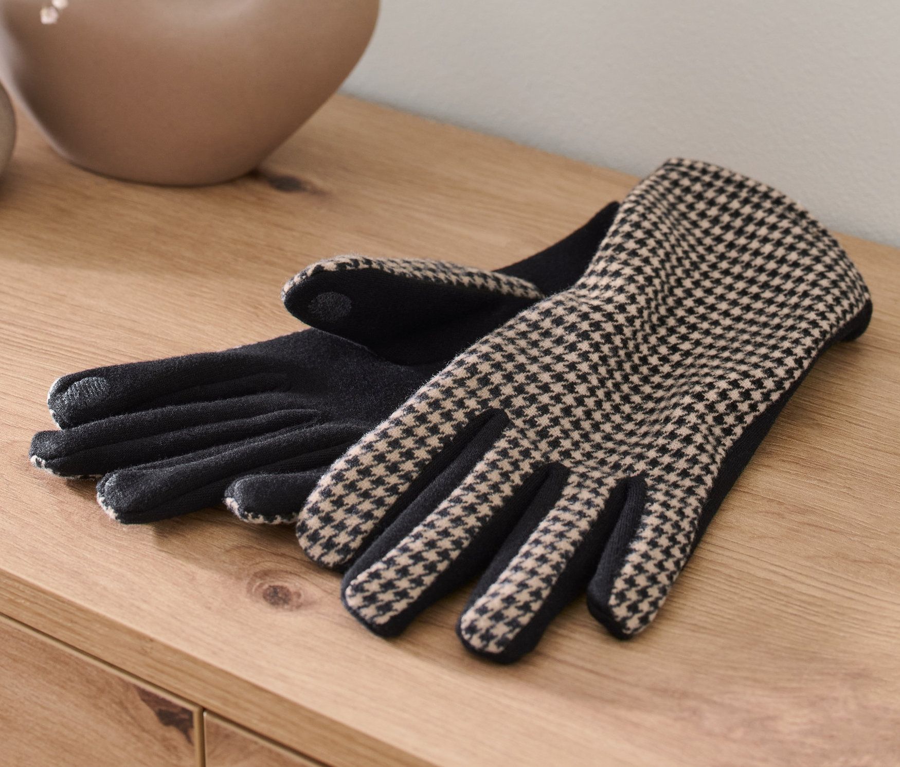 Dvoje rukavice zo zmesi materiálov ležia na drevenom stole vedľa vázy s kvetmi.