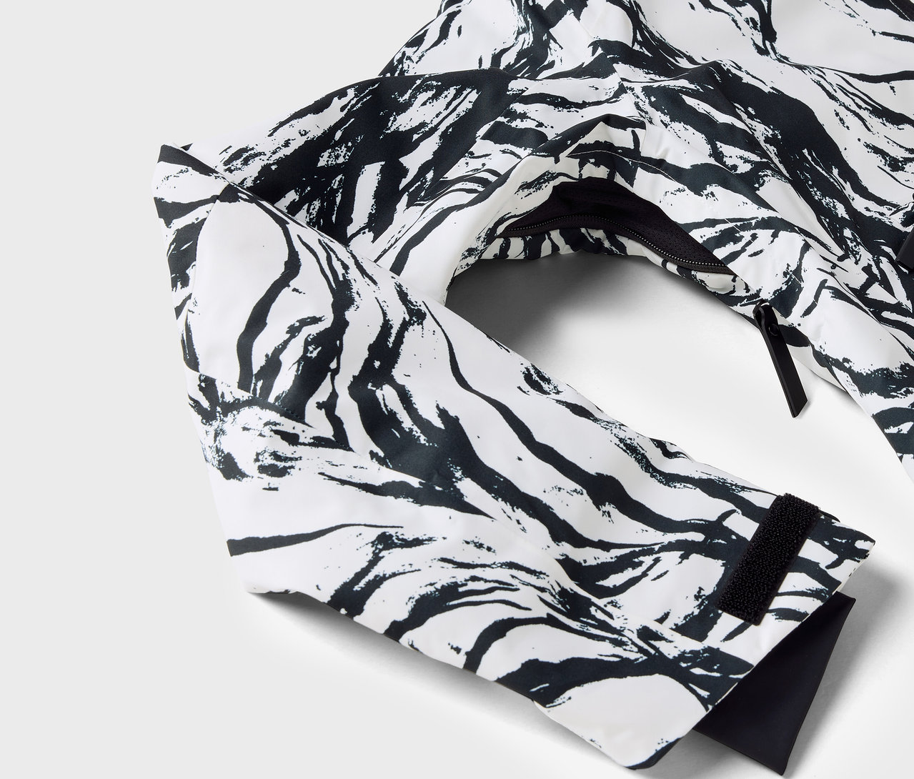 Detail bielej bundy s čiernym vzorom, viditeľný rukáv a zips.