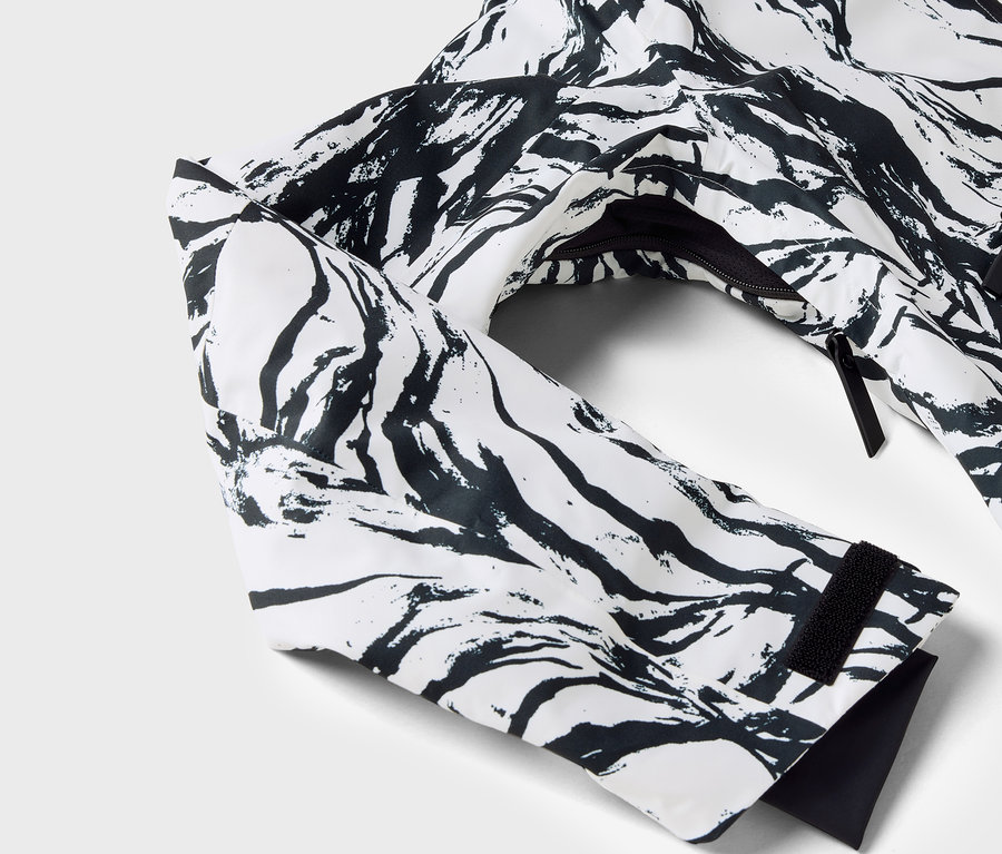 Detail bielej bundy s čiernym vzorom, viditeľný rukáv a zips.