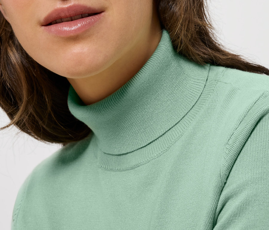 Detail dámy s hnedými vlasmi v mätovo zelenom roláku.