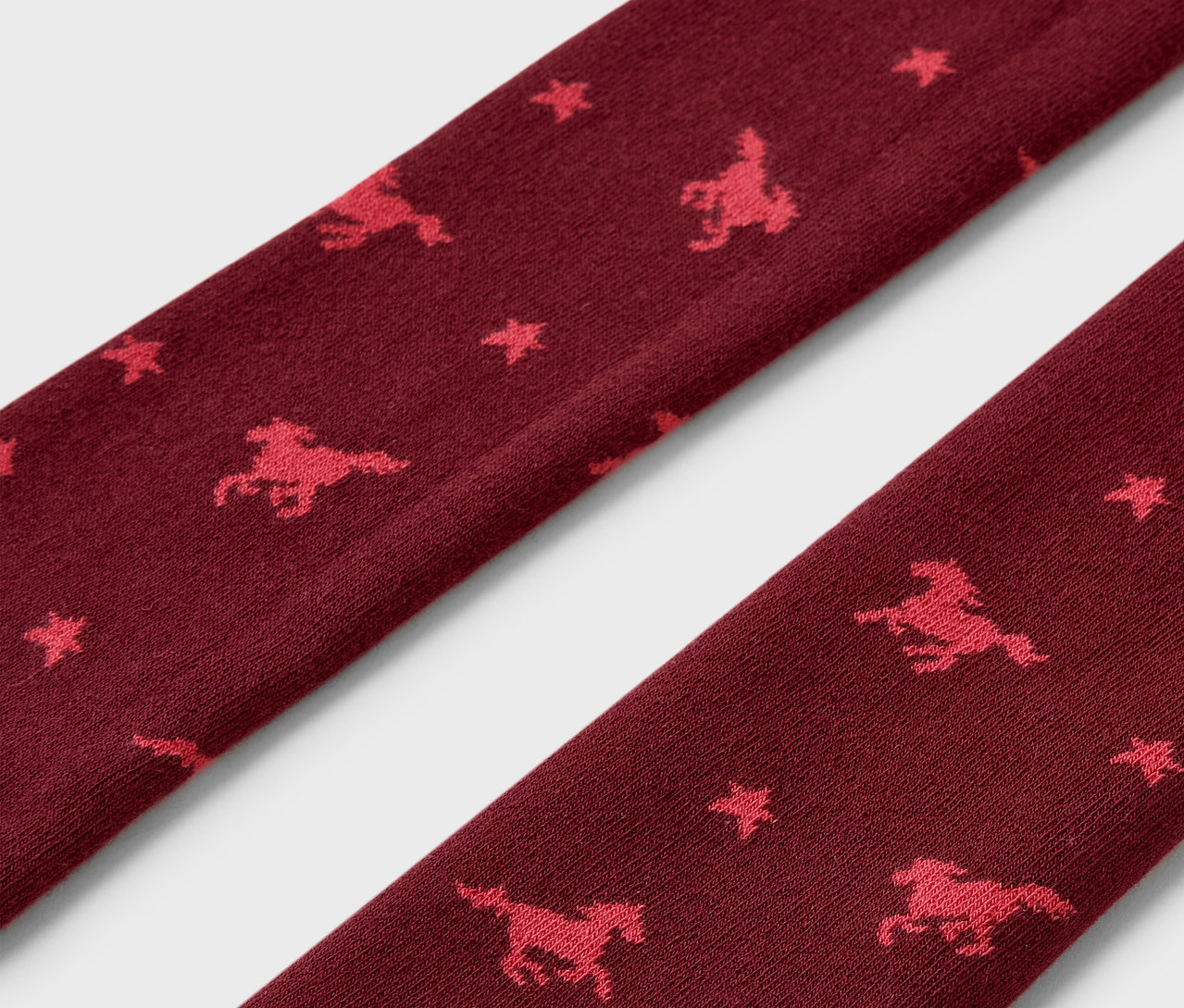 Detail bordových termo legín so vzorom koní a hviezd.