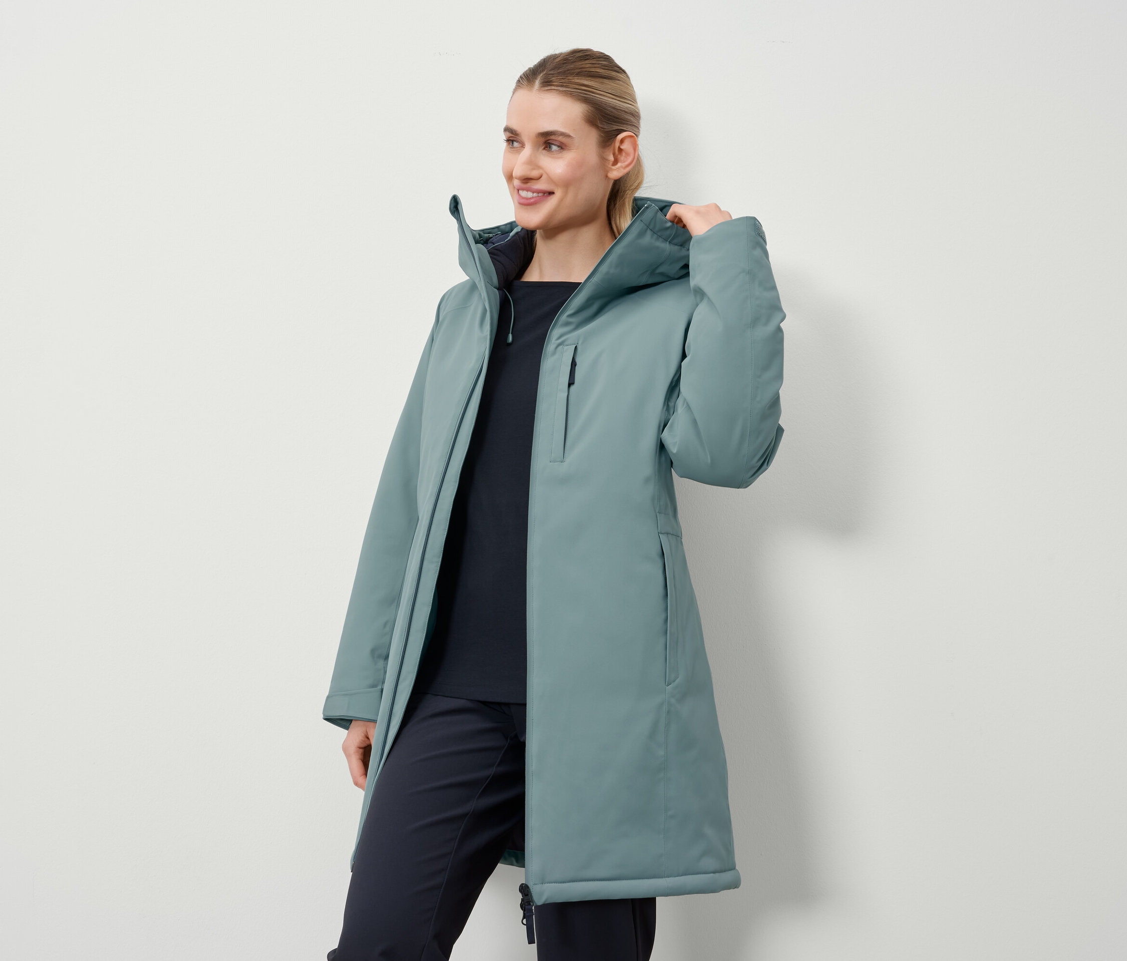 Žena má na sebe dlhý kabát petrolejovej farby.