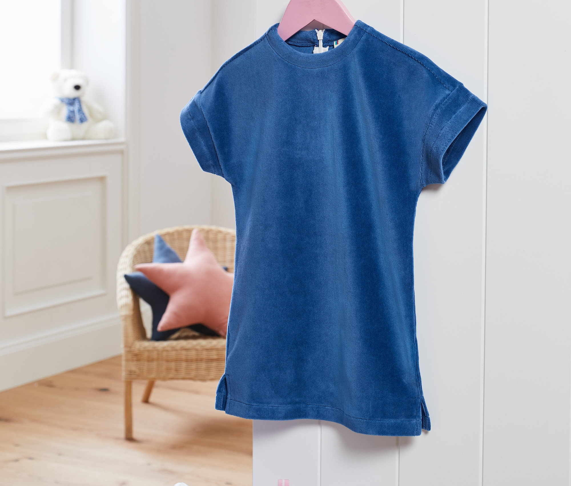 Modré elastické menčestrové šaty visia na ružovom vešiaku.