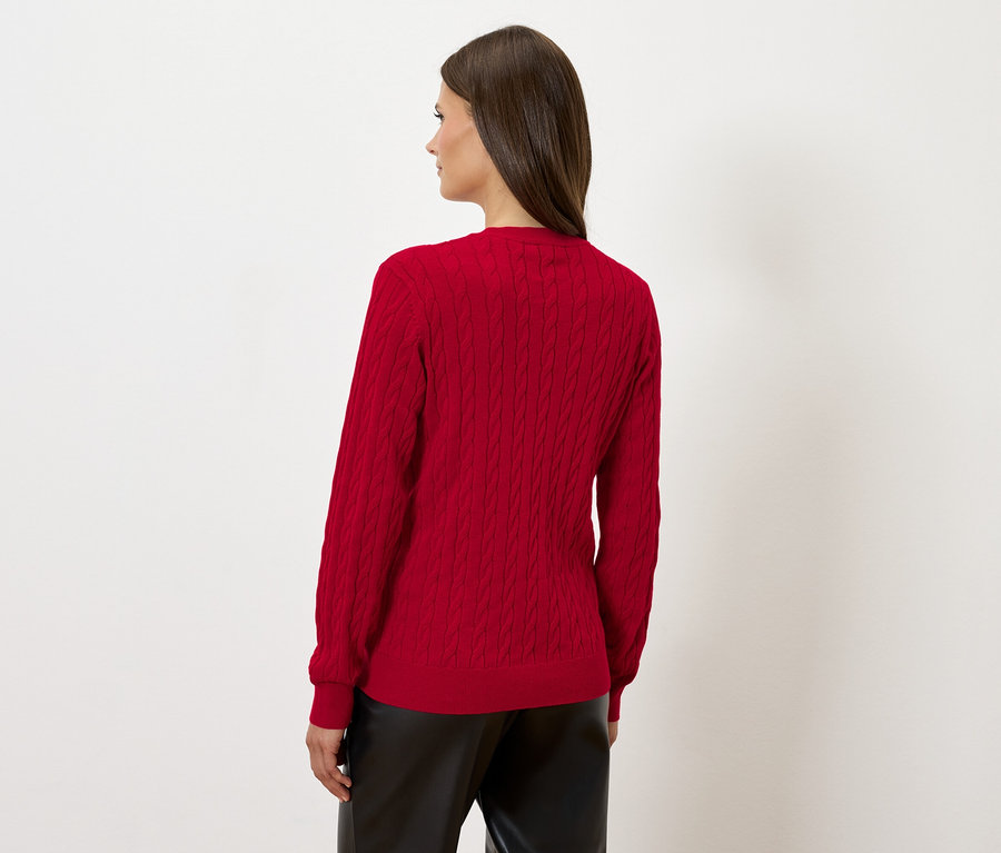 Žena stojí chrbtom a má na sebe červený sveter a čierne kožené nohavice.