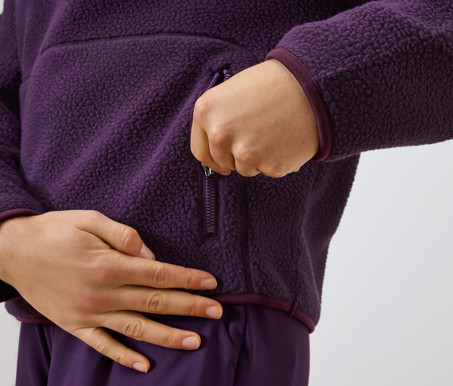 Osoba zatvára zips na fialovej flísovej mikine.
