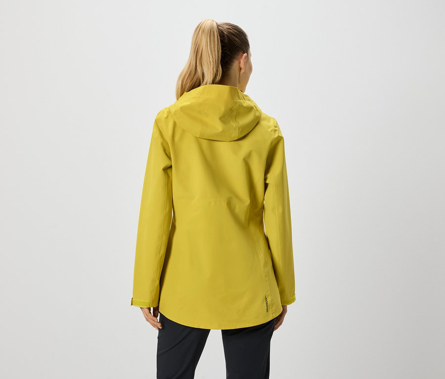 Pohľad zozadu na ženu s copom v horčicovo žltej bunde s kapucňou a čiernych nohaviciach.