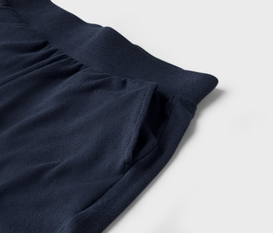 Detail tmavomodrých teplákov s vreckom na bielom pozadí.