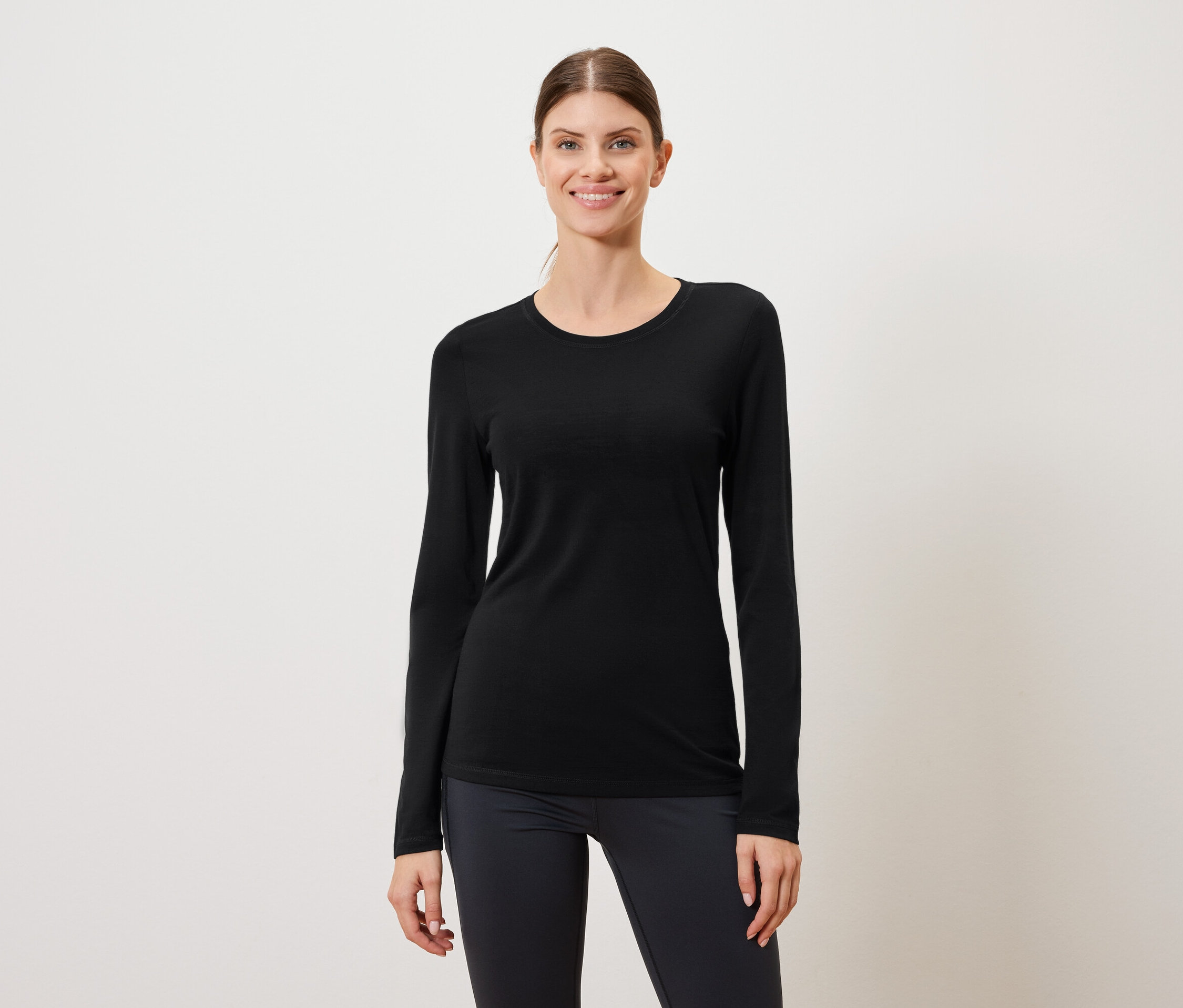 Žena má na sebe čierne tričko s dlhým rukávom a tmavé legíny na bielom pozadí.