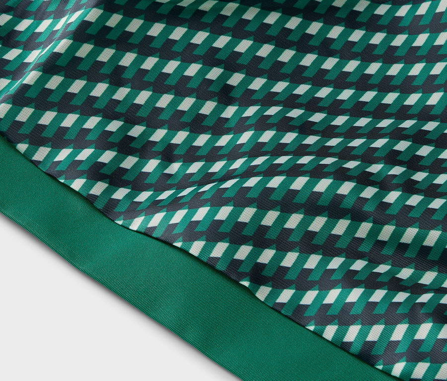 Detail látky s geometrickým vzorom v zelených, bielych a čiernych tónoch a zelenou stuhou.