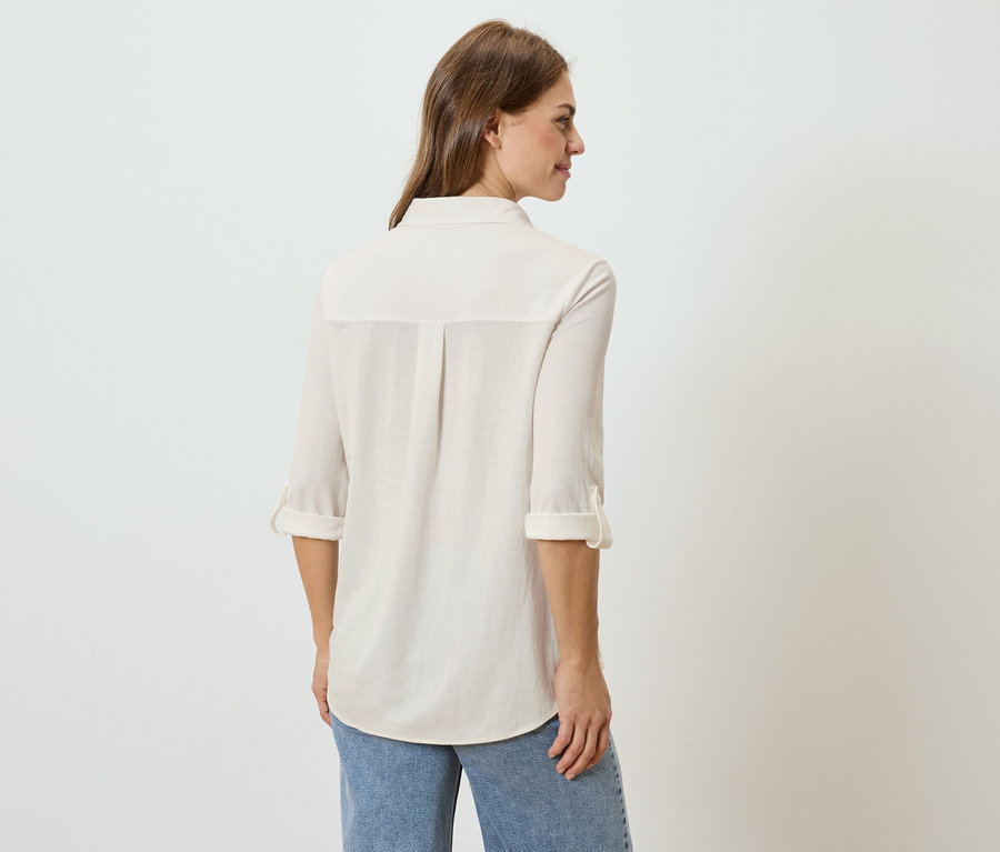 Pohľad zozadu na ženu s dlhými hnedými vlasmi, oblečenú vo svetlej košeli a džínsoch.