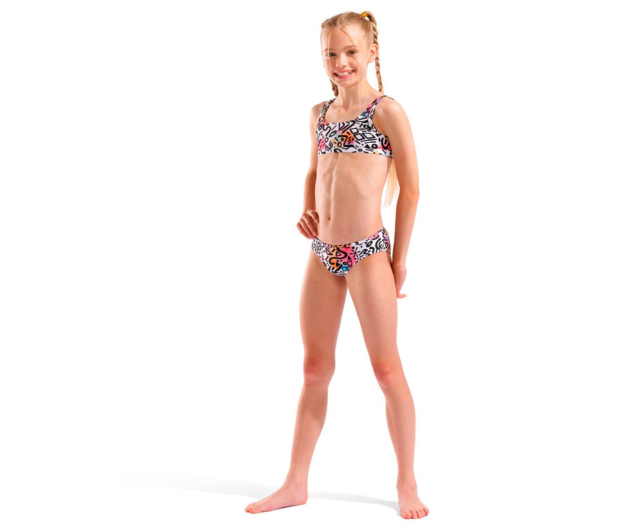 Dievča s blond vrkočmi, ktoré má na sebe biele bikiny s farebným vzorom a usmieva sa.