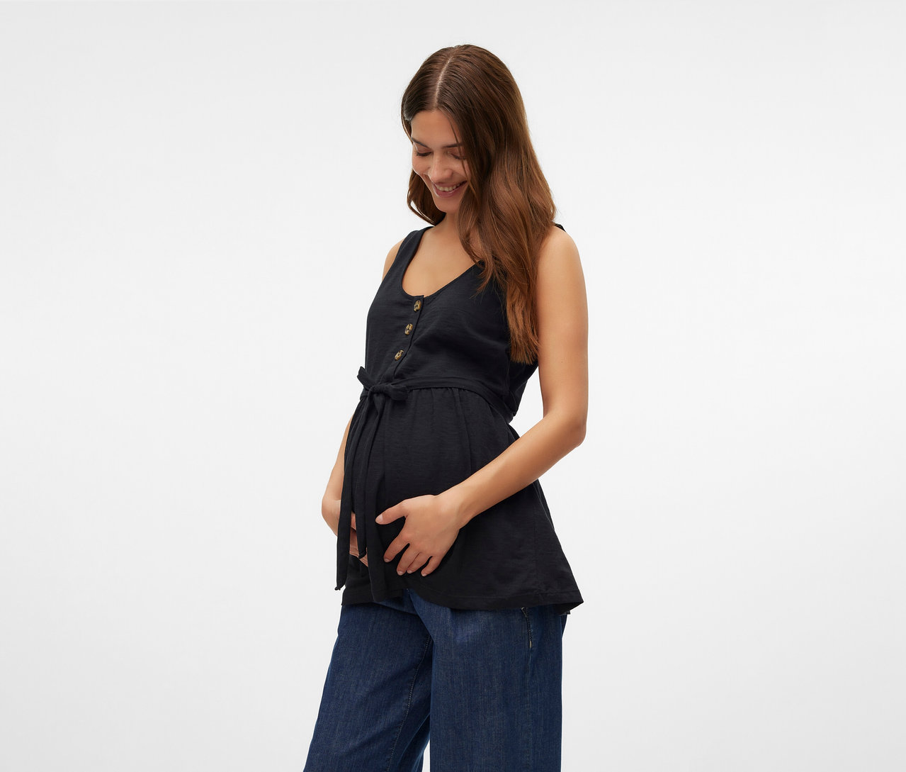 Žena drží si brucho a má na sebe čierny top MAMALICIOUS »MLEVI LIA« a široké džínsy.