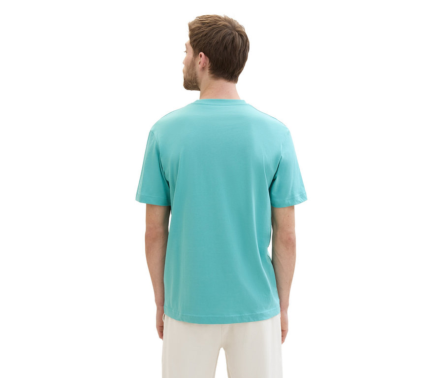 Muž zozadu v tričku s logom Tom Tailor, meadow teal a svetlých nohaviciach.
