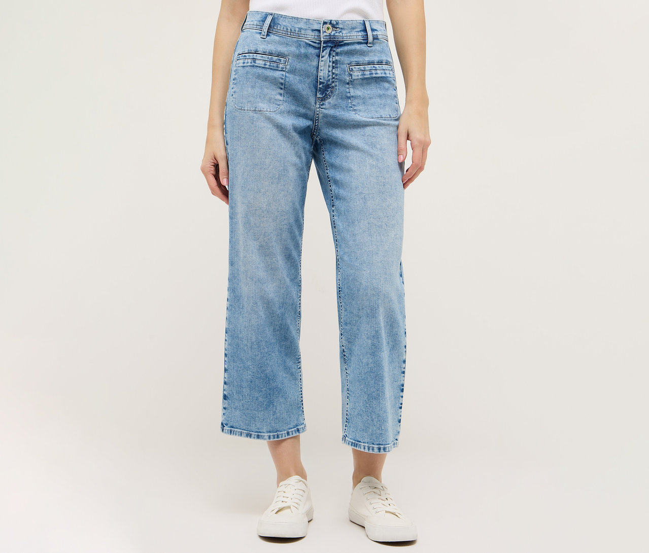 Žena má na sebe svetlomodré nohavice Angels Denim »Linn Smart« Culotte a biele topánky na bielom pozadí.