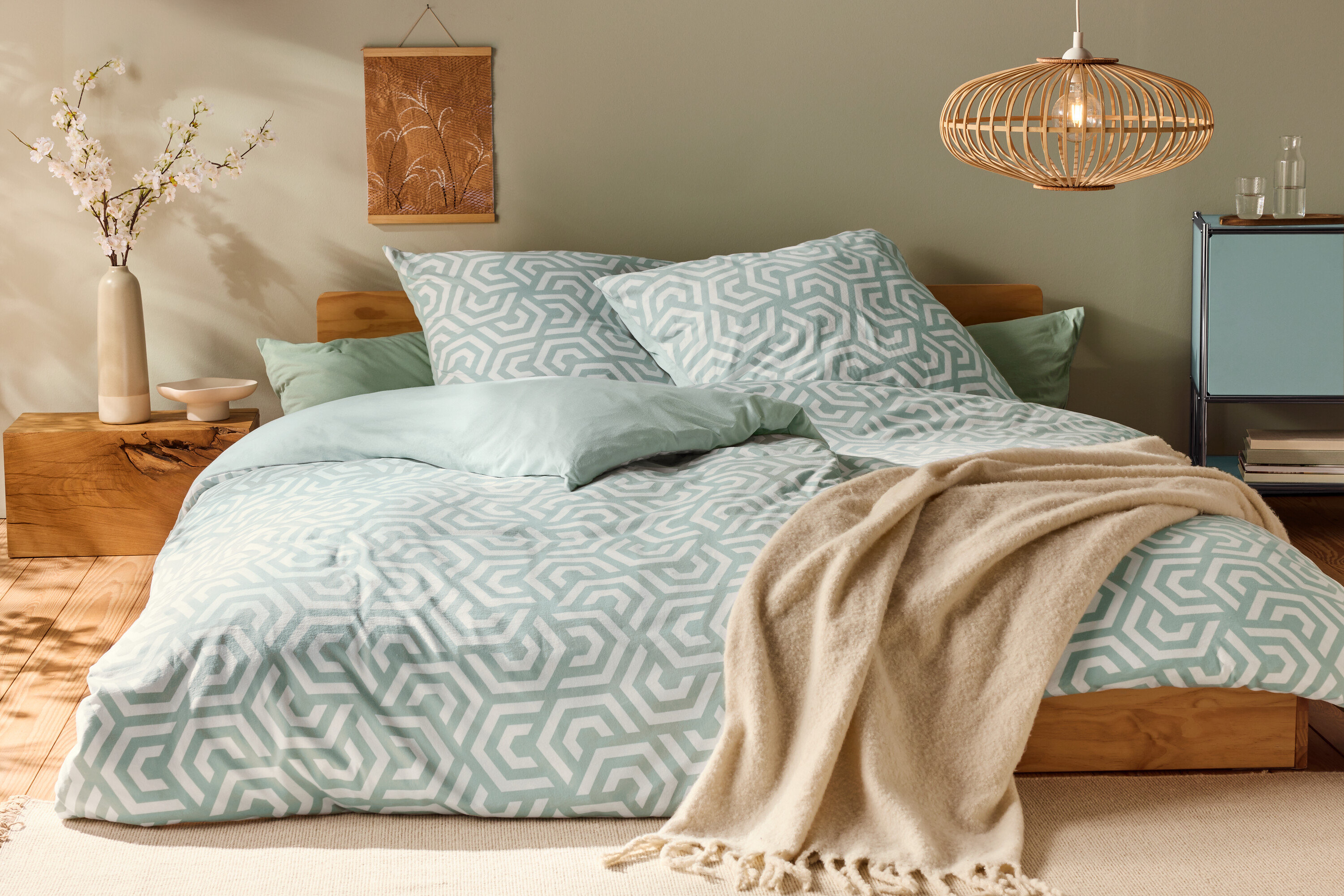 Posteľ s džersejovou posteľnou bielizňou štandardnej veľkosti s geometrickým vzorom a svetlozelenými vankúšmi.