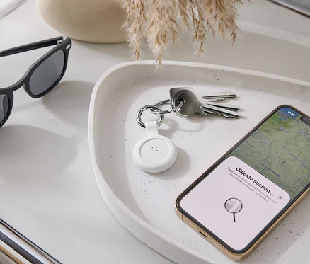 Na podnose ležia slnečné okuliare, kľúče, biely tracker a smartfón s mapovou aplikáciou.