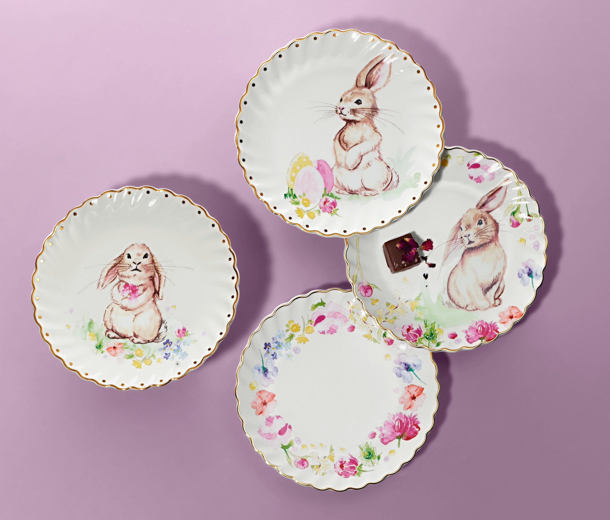 Štyri dezertné taniere s lesklým zlatým dekorom a obrázkami zajačikov na fialovom pozadí.