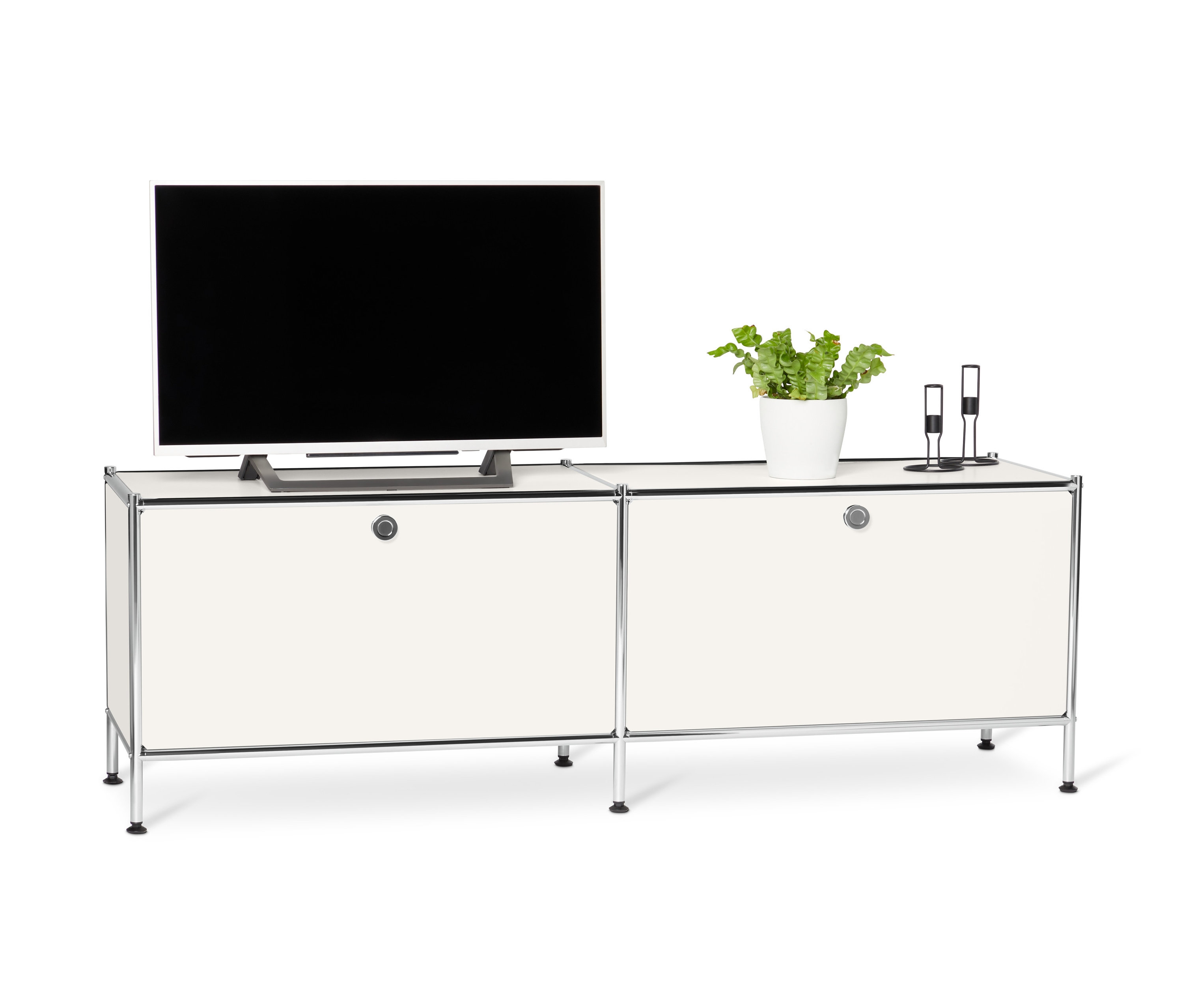 Televízor stojí na bielej kovovej nízkej skrinke »CN3« s výklopnými priehradkami.