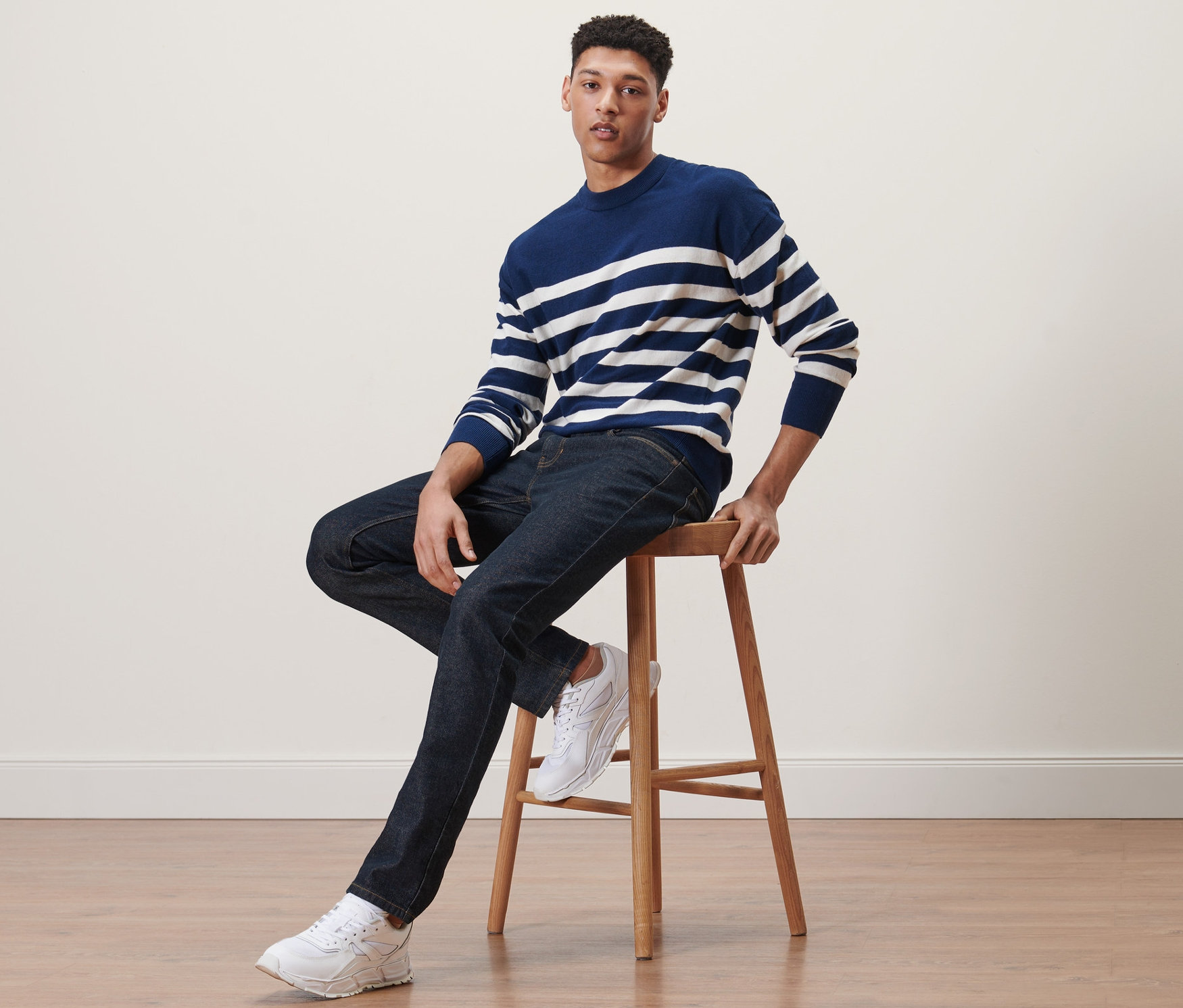 Muž sedí na stoličke a má na sebe džínsy.