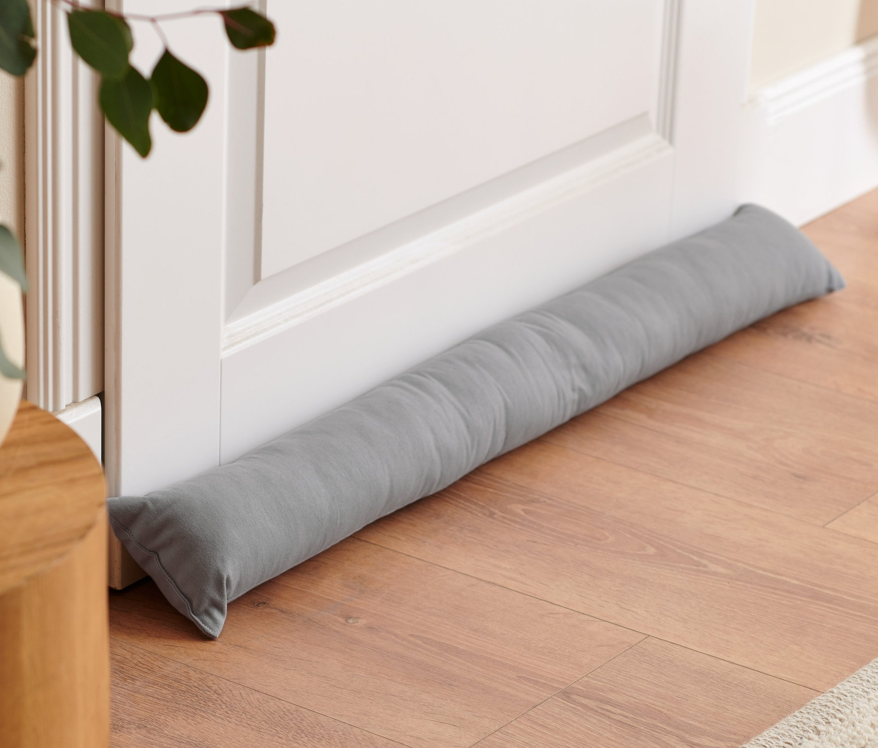 Sivá ochrana proti prievanu leží pri spodnej časti bielych dverí na drevenej podlahe.