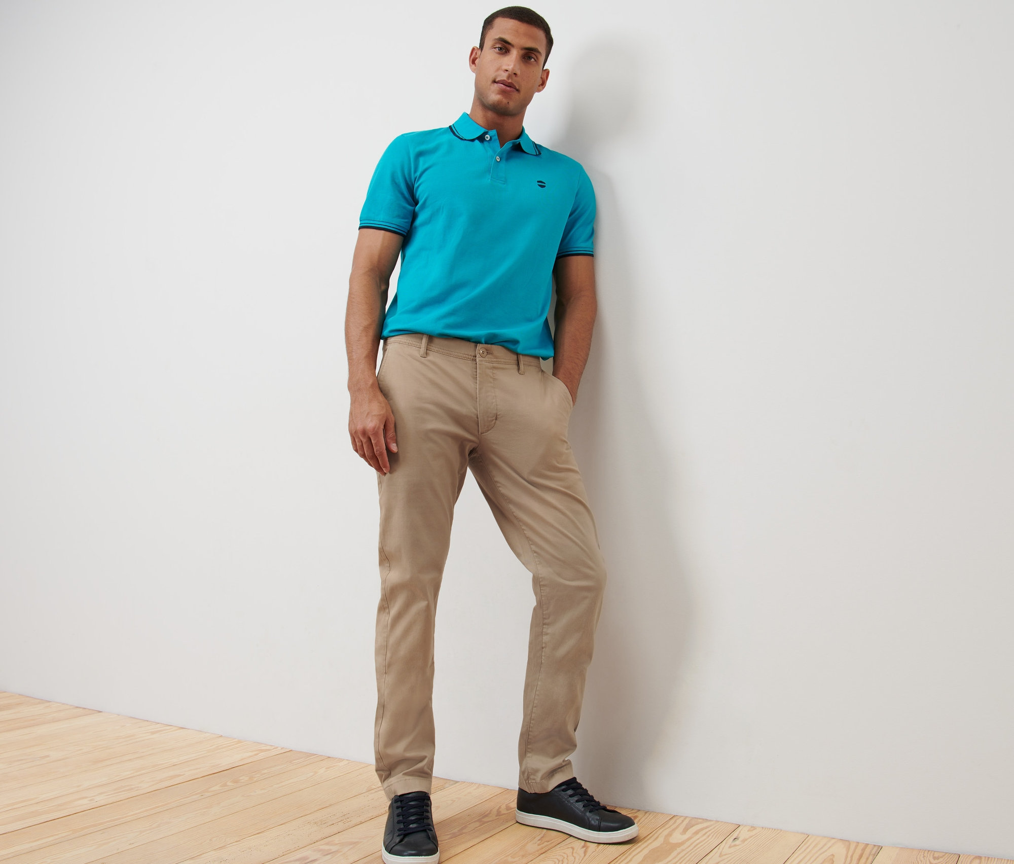 Muž pózuje v béžových chino nohaviciach a modrej polokošeli.