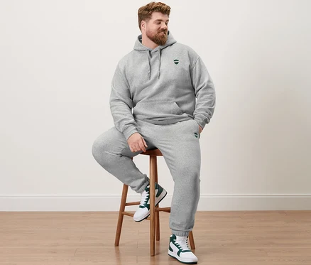 Muž sedí na stoličke v sivej melírovanej mikine s kapucňou a teplákových nohaviciach.