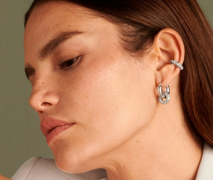 Žena sedí a má na sebe náušnicu Sparkle Donut, prsteň Sparkle Donut, kreoly Sparkle Donut a retiazku Sparkle Donut.