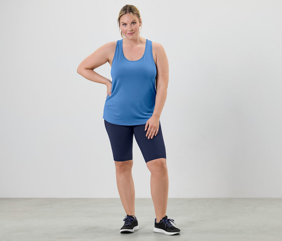 Žena pózuje vo funkčnom tope azúrovej farby z dvojdielnej súpravy a v cyklistických šortkách.