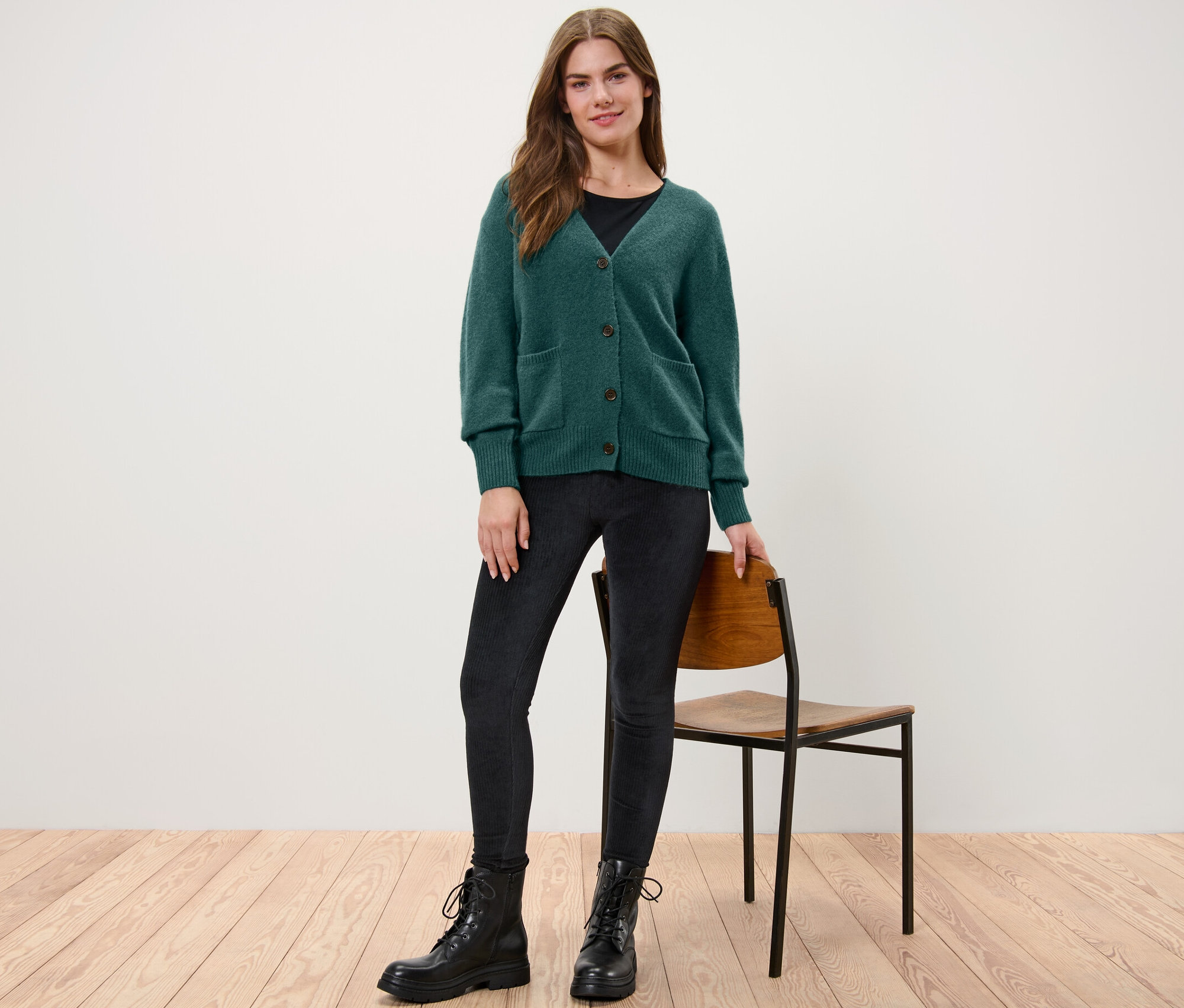 Žena stojí a má na sebe tmavozelený pletený sveter s vlnou.
