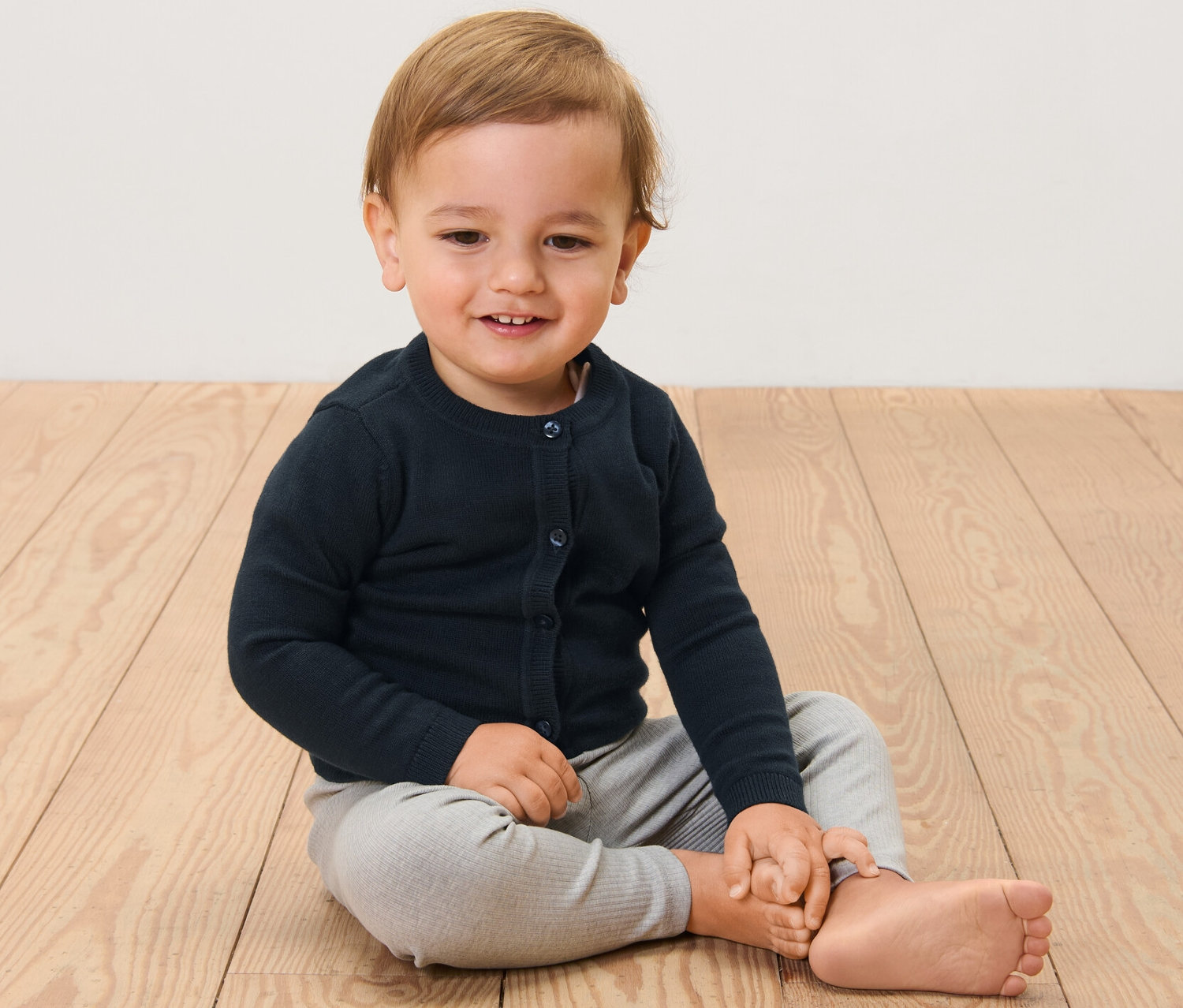 Dieťa sedí na drevenej podlahe a má na sebe detský svetrík.
