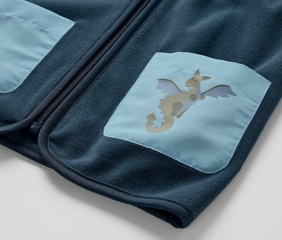 Detailný pohľad na detskú flaušovú vestu, drak, s modrou nášivkou draka na vrecku.