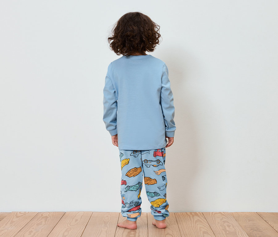 Dieťa chrbtom k fotoaparátu má na sebe modré pyžamo s potlačou autíčok.