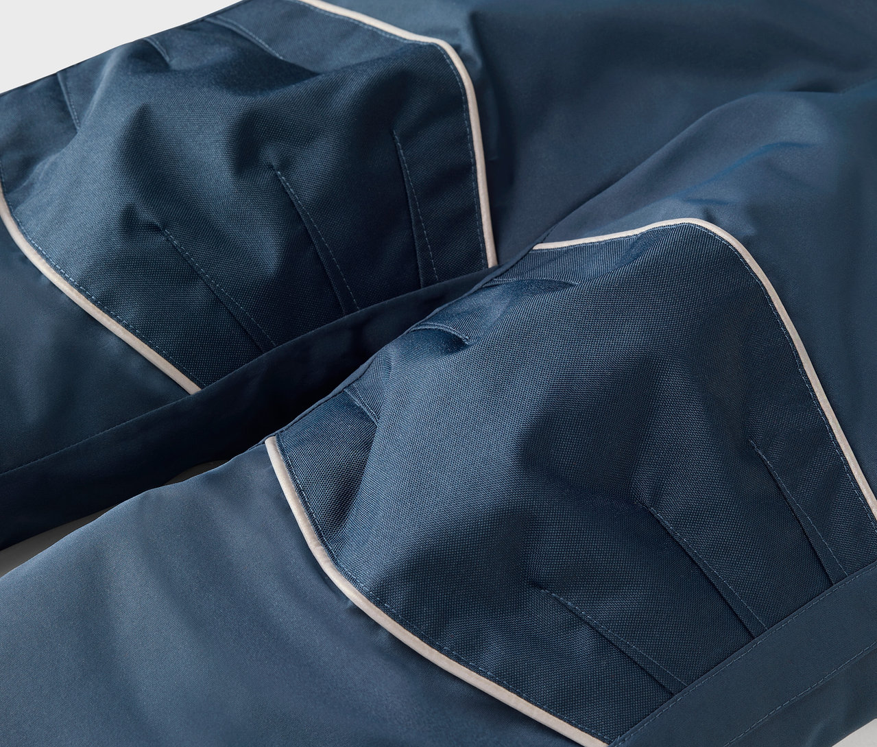 Detail modrých nohavíc s bielym lemovaním a vreckami.