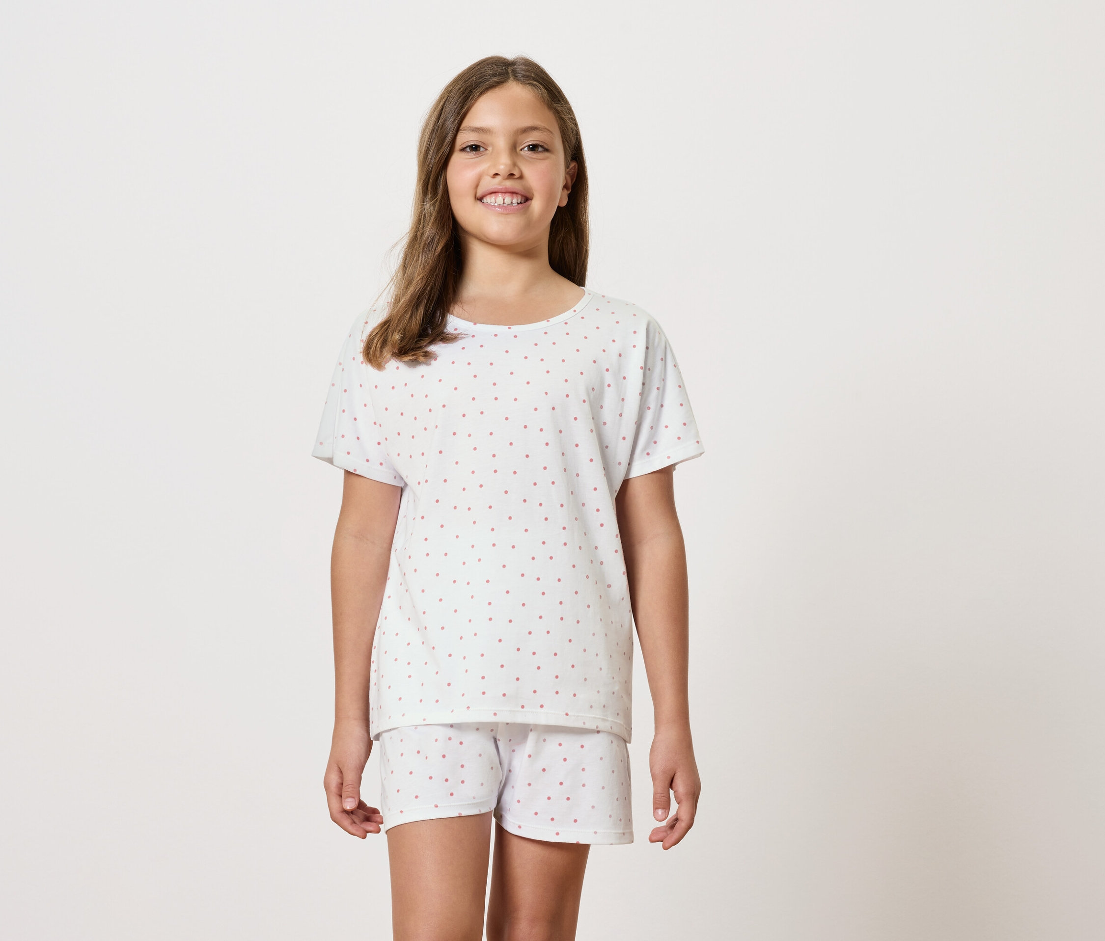 Dievča má na sebe biele pyžamo s krátkym rukávom a šortkami.