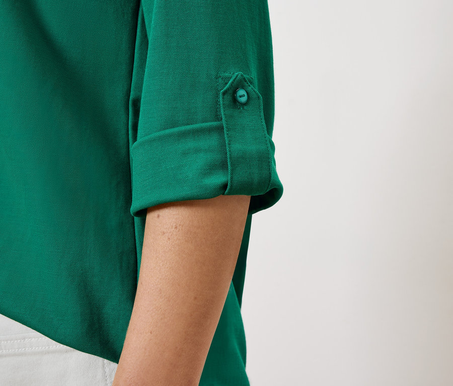 Detail dámskej zelenej košele s vyhrnutými rukávmi a gombíkom.