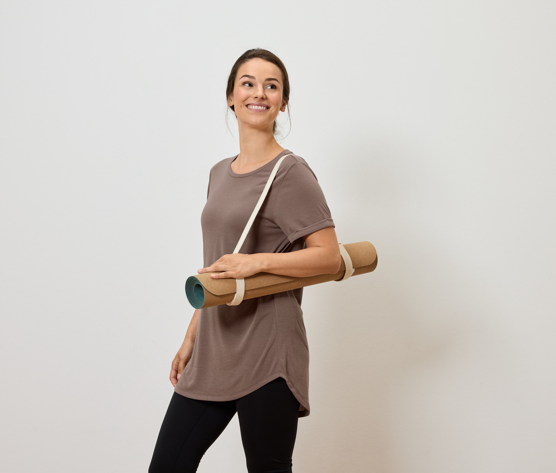 Usmievajúca sa žena nesie podložku na jogu cez rameno.