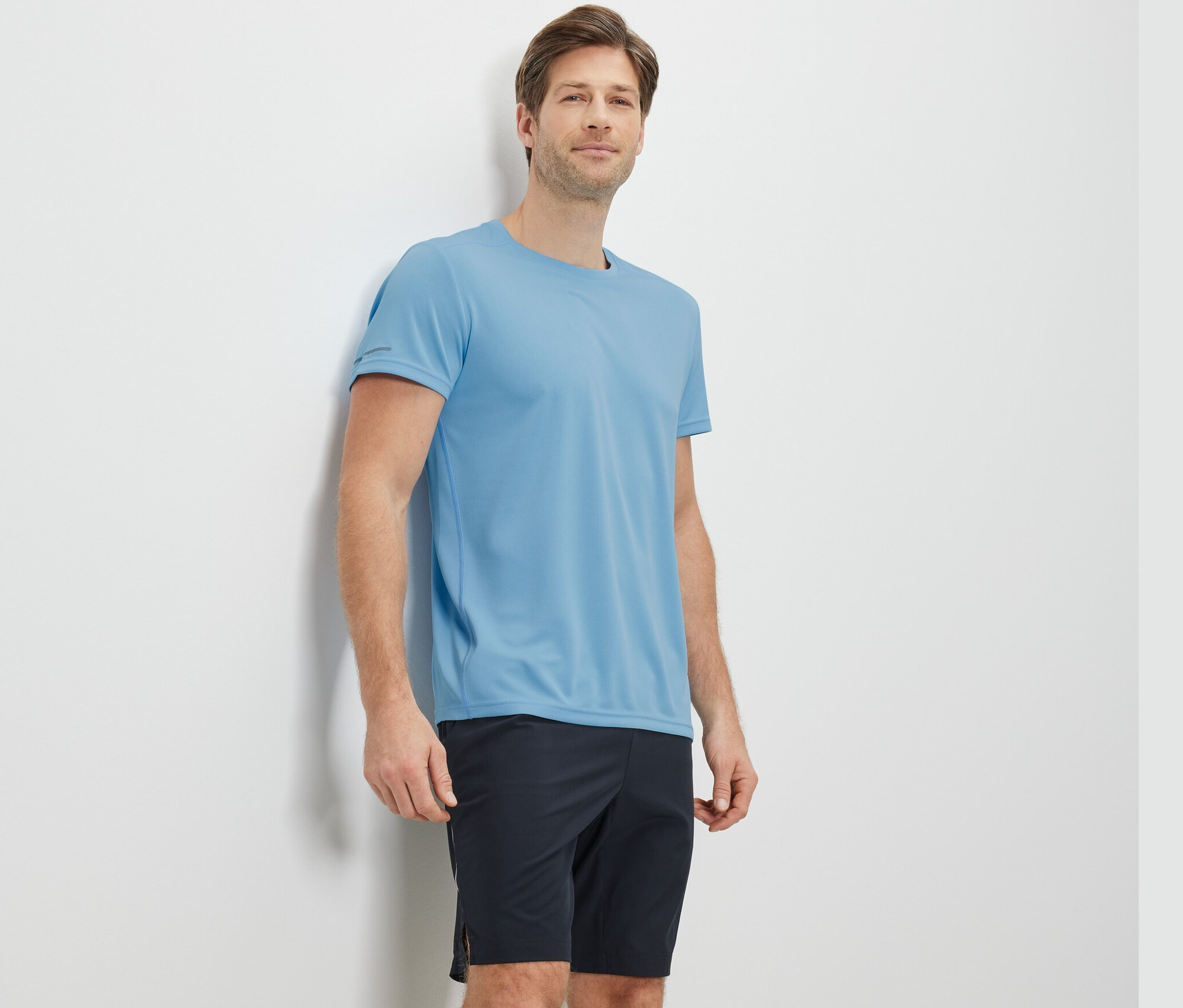 Muž opretý o stenu má na sebe svetlomodré funkčné tričko.