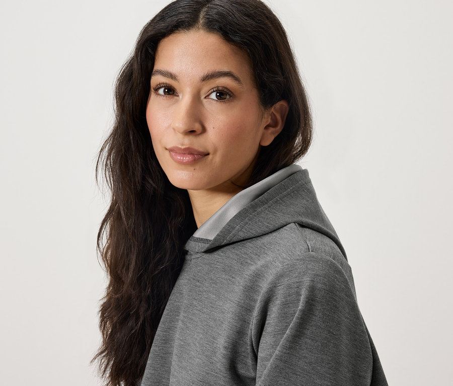 Portrét ženy s dlhými tmavými vlasmi v šedej mikine s kapucňou.