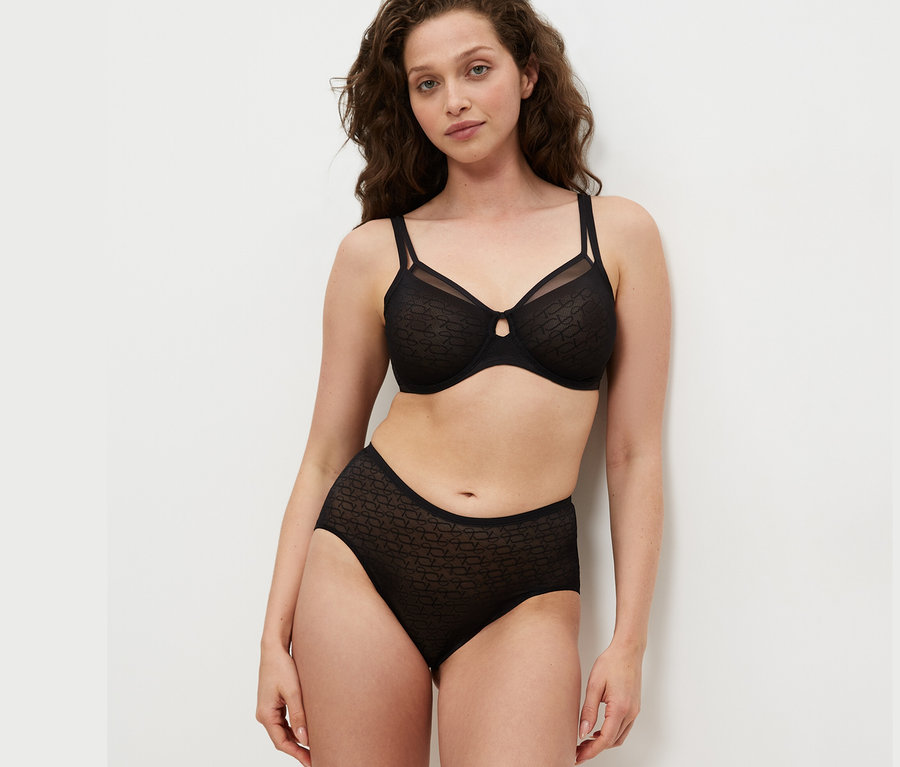 Žena má na sebe čiernu podprsenku Triumph Signature Sheer Minimizer a čierne nohavičky.