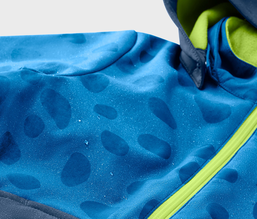 Detail modrej detskej softshellovej bundy meniacej farbu v daždi so zeleným zipsom.