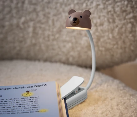 Lampa na čítanie v tvare medveďa pripnutá ku knihe.