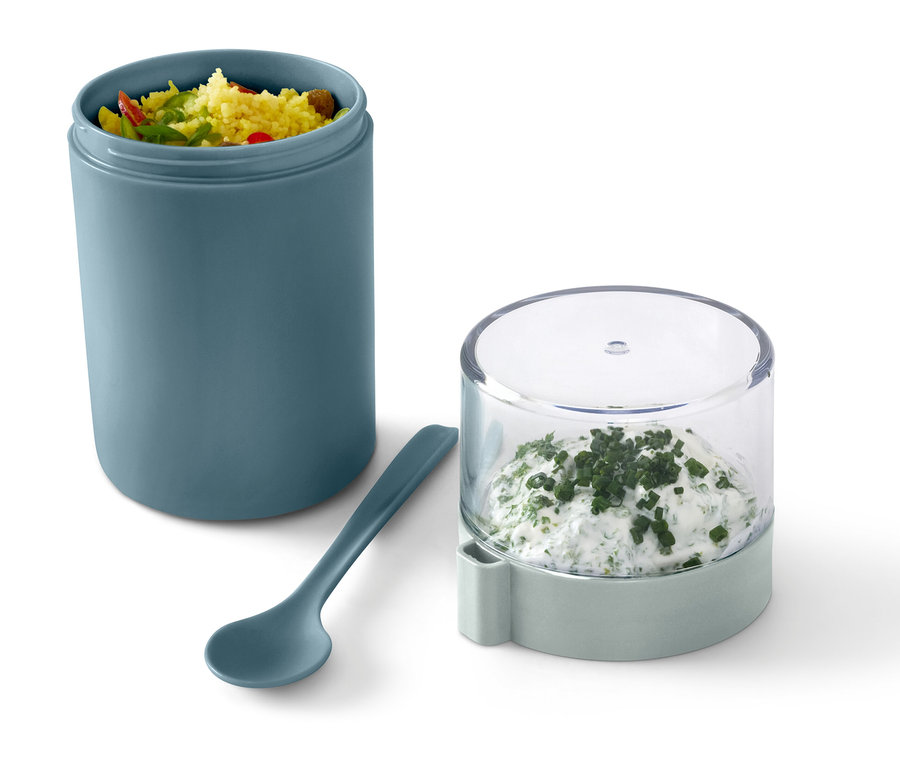 Zelený cestovný pohár na jogurt s obsahom, vedľa lyžica a nádoba s bylinkovou nátierkou.