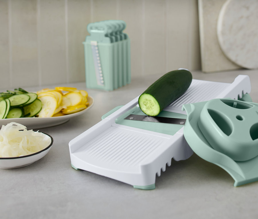 Zelená uhorka na bielom krájači zeleniny s príslušenstvom. Na tanieri sú nakrájané uhorky a žltá tekvica.