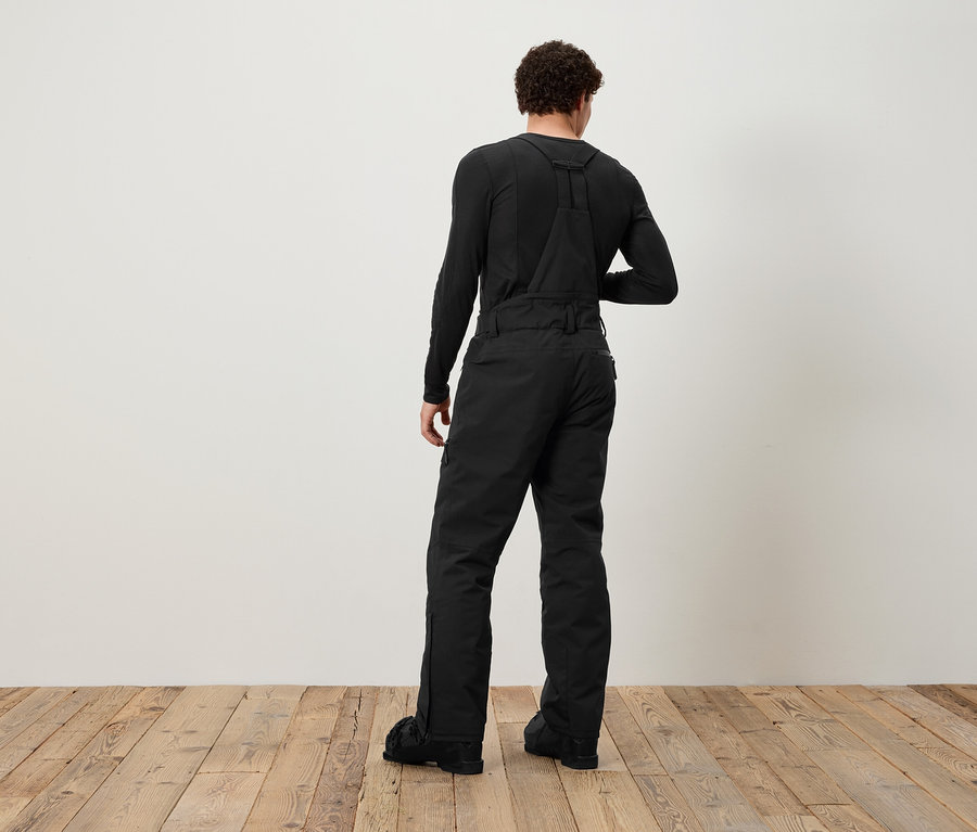 Muž chrbtom k fotoaparátu má na sebe čierne traky a čierne tričko s dlhým rukávom.