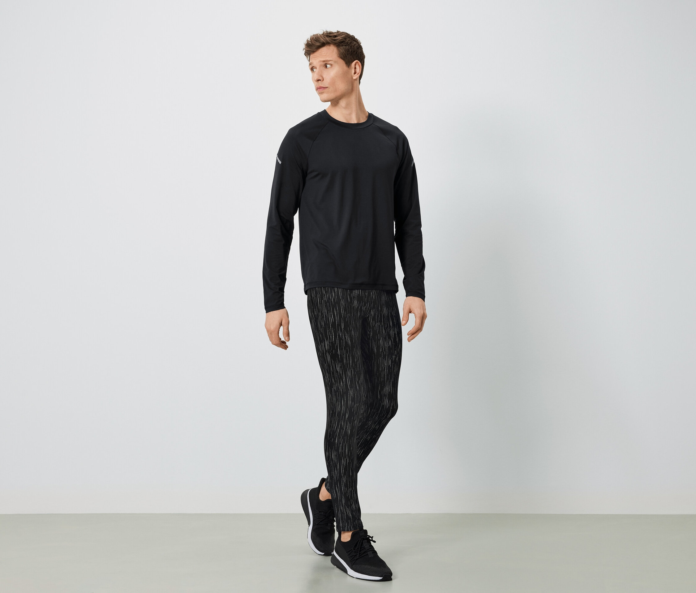 Muž v čiernom športovom oblečení pózuje na svetlom pozadí.