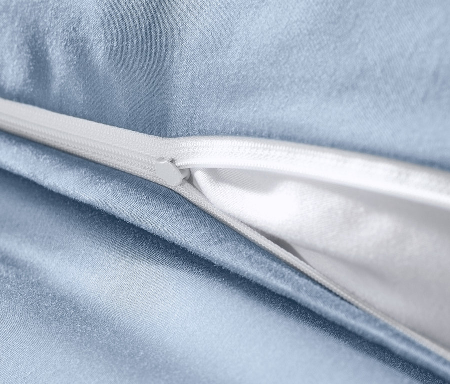 Detail svetlomodrej posteľnej bielizne z bavlny a saténu s bielym zipsom.