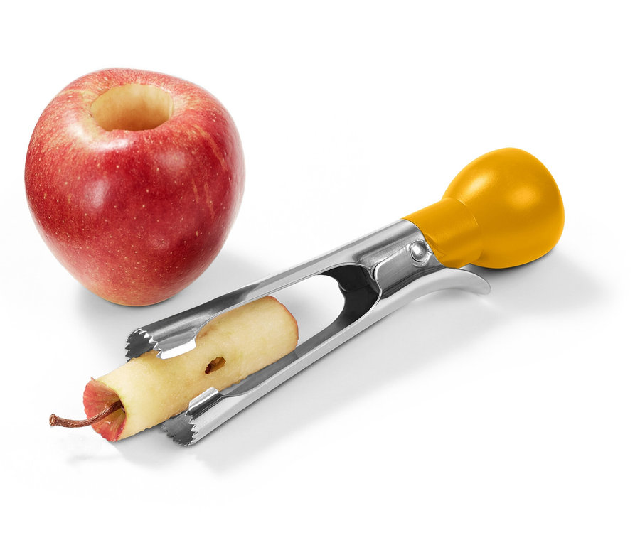 Červené jablko s vydlabaným stredom stojí vedľa nerezového odstraňovača jadierok so žltou rukoväťou, ktorý odstraňuje jadro z druhého jablka.